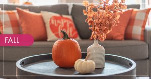 A living room with a grey couch decorated with orange fall pillows and a coffee table with pumpkins and fall leaves in a vase.