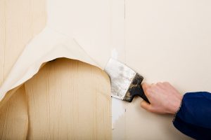 hand removing wallpaper with a scraping tool